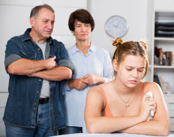 Upset female is sitting at the table and her parents are sympathying with her at home.
